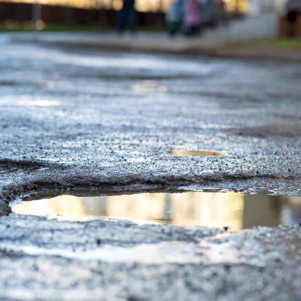 Close up of a road in very bad condition with big potholes full of dirty rain water pools.